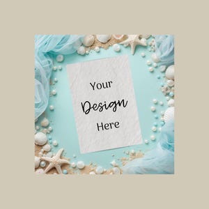 May include: A blank white card with the text "Your Design Here" is surrounded by seashells, pearls, sand, and blue fabric on a light blue background. The composition evokes a beach or ocean theme.