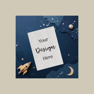 May include: A white rectangular card with the text "Your Design Here" in black script is centered on a dark blue background with a space theme. A small wooden rocket, a silver sphere, and a wooden crescent moon are also present.