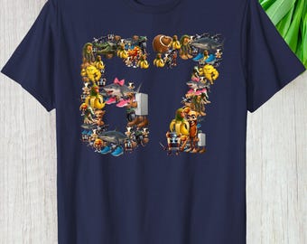 May include: Navy blue t-shirt featuring the number "67" composed of various cartoon characters and objects. The design includes sharks, bananas, and other colorful illustrations. A casual, graphic tee.