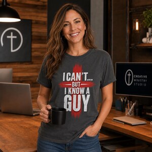 May include: A charcoal grey short-sleeve t-shirt featuring a distressed red cross graphic behind the white text that reads I CAN'T... BUT I KNOW A GUY. The shirt has a crew neckline and a standard fit, made from a soft, worn-in fabric material.