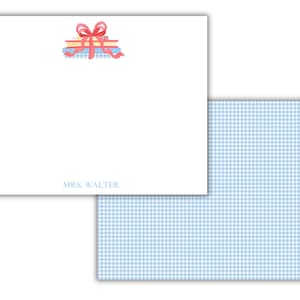 May include: A white stationery card featuring a watercolor illustration of a stack of books tied with a red ribbon bow at the top. The text MRS. WALTER is printed in light blue at the bottom. A matching light blue and white gingham envelope liner.
