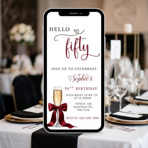 Puede incluir: Un teléfono inteligente muestra una invitación de cumpleaños. El texto "HELLO fifty" está escrito en una fuente de guion. La invitación es para un 50 cumpleaños, con una copa de champán y un lazo rojo.
