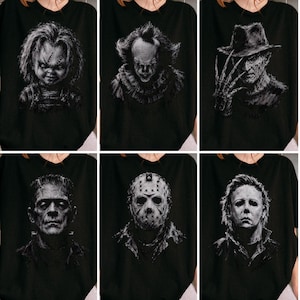 May include: A black t-shirt featuring a collage of six iconic horror movie characters printed in a monochromatic, sketch-like style. The graphic includes Chucky, Pennywise, Freddy Krueger, Frankenstein's monster, Jason Voorhees, and Michael Myers.