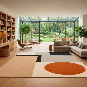 May include: A rectangular area rug featuring a geometric pattern with a large burnt orange circle, a black rectangle, and blocks of beige, tan, and light gray on a light wood floor in a living room with a bookshelf, sofa, and glass wall.