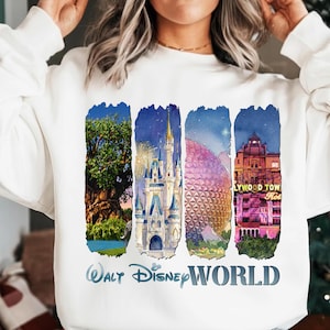 May include: White sweatshirt featuring a watercolor design of Walt Disney World landmarks. The design includes the Tree of Life, Cinderella Castle, Spaceship Earth, and the Hollywood Tower Hotel. The words "Walt Disney World" are printed below the images.