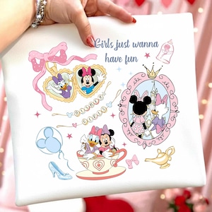 May include: White tote bag featuring Disney characters Minnie Mouse and Daisy Duck. The bag has a pink bow, a heart-shaped locket, and the text "Girls just wanna have fun." Other graphics include a teacup, a glass slipper, and a castle.