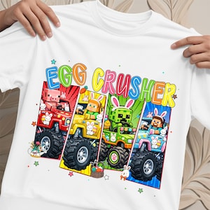 May include: White t-shirt featuring the text "EGG CRUSHER" in colorful letters. The design includes four monster trucks with Easter-themed characters and bunnies. The trucks are red, yellow, green, and blue.