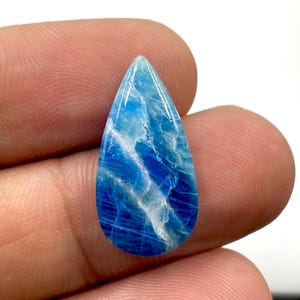 May include: A teardrop-shaped blue gemstone featuring a polished surface with distinct white veining and deep azure color variations throughout the stone. The gem displays a smooth, glossy finish with a translucent quality and a pointed top.
