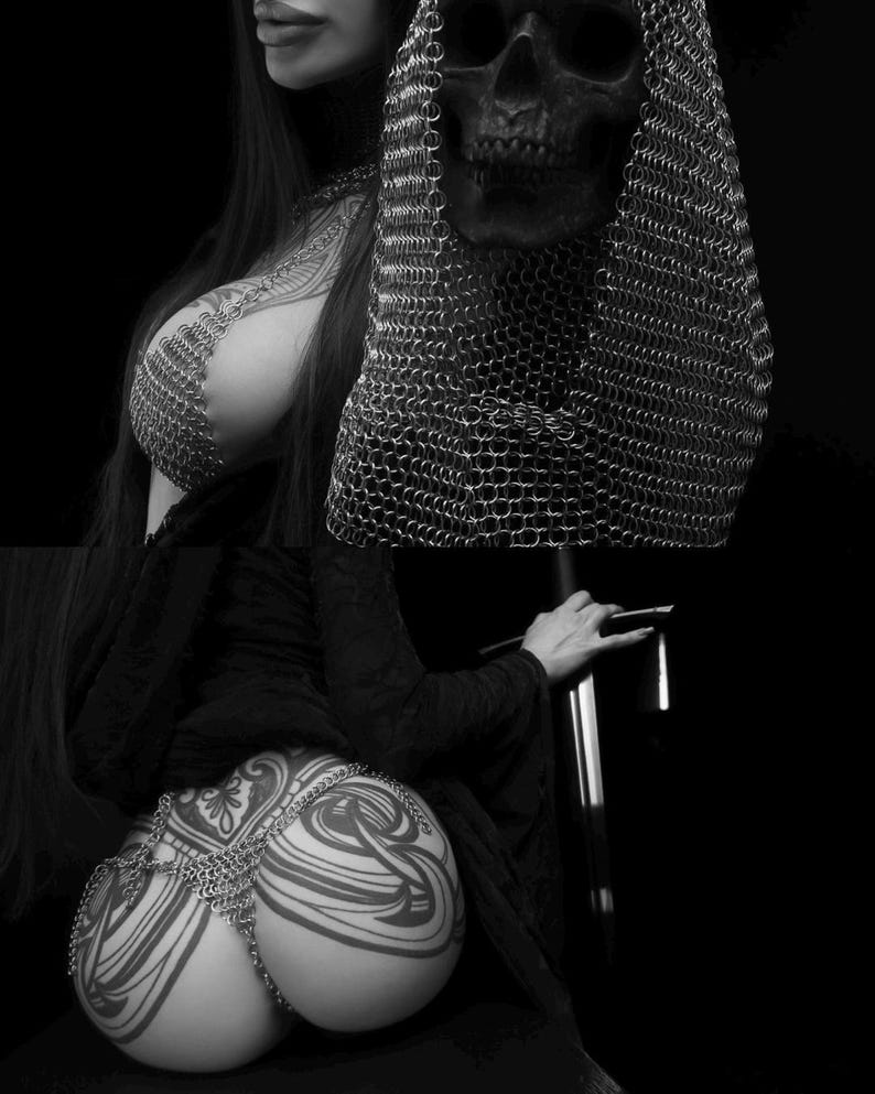 May include: Black and white image featuring a skull wearing a chainmail hood. The image also shows a person with tattoos and chainmail body jewelry. The person is holding a sword. The overall theme is gothic and dark.