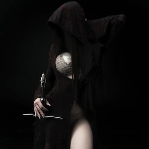 May include: A figure in a dark hooded cloak and a chainmail top, holding a sword against a black background. The cloak is a deep burgundy color, and the sword has a silver blade. The image has a gothic or fantasy theme.