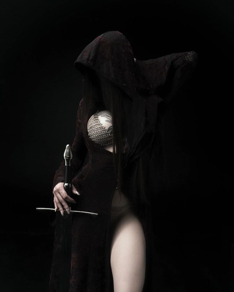 May include: A figure in a dark hooded cloak and a chainmail top, holding a sword against a black background. The cloak is a deep burgundy color, and the sword has a silver blade. The image has a gothic or fantasy theme.