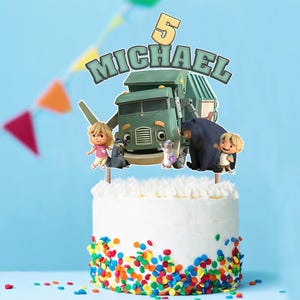 以下が含まれることがあります： ベースにカラフルなスプリンクルをあしらった白いフロストケーキ。ケーキの上には、緑色の漫画のゴミ収集車、キャラクター、数字の5、そして「MICHAEL」という名前が飾られています。カラフルな三角形のバナーが背景にぶら下がっています。