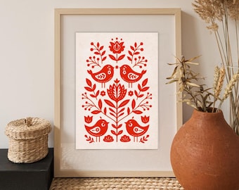 May include: Framed art print featuring a red folk art design of birds and floral elements on an off-white background. The artwork is displayed in a light wood frame, adding a touch of rustic charm to the decor. The print is a decorative piece.