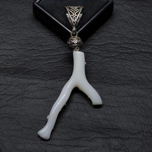 May include: White coral branch pendant with a silver-toned bail and decorative bead. The pendant is displayed on a black surface. The coral branch has a natural, organic shape.