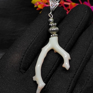 May include: A white coral pendant with a silver bail and decorative beads. The coral has a branching structure with a smooth, polished surface. The pendant is displayed against a black background, with colorful flowers in the background.