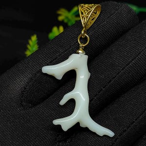 May include: A white coral pendant with a gold-colored bail. The coral has a branch-like shape with multiple offshoots. The pendant hangs from a small gold-colored ring. The background is black.