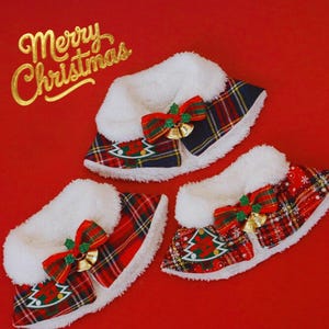 Puede incluir: Tres collares navideños para mascotas con un estampado de cuadros rojos y verdes, ribete de piel sintética blanca y un lazo rojo con campanas doradas. Los collares tienen un diseño de árbol de Navidad y las palabras "Merry Christmas" en dorado.