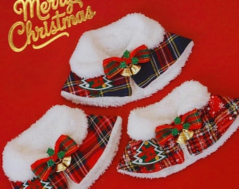 May include: Three Christmas-themed pet collars with a red and green plaid pattern, white faux fur trim, and a red bow with gold bells. The collars have a Christmas tree design and the words "Merry Christmas" in gold.