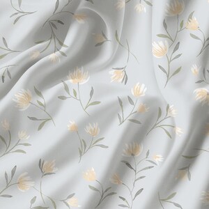 May include: A light blue fabric with a repeating floral pattern. The flowers are a soft yellow with green stems and leaves. The fabric has a subtle sheen and is draped in soft folds.