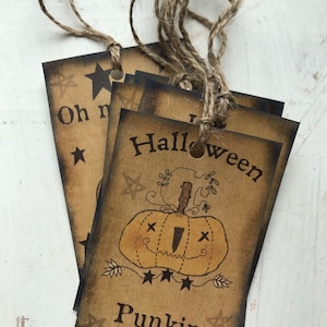 May include: A stack of brown paper tags with a rustic, vintage aesthetic. Each tag features a black-ink illustration of a jack-o'-lantern and the words "Halloween" and "Punkin Patch". The tags are tied together with twine.