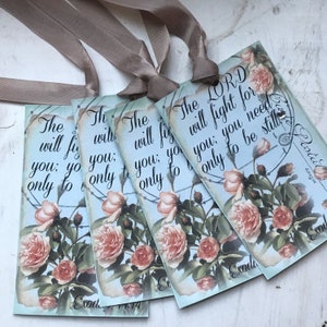 May include: Four blue and white floral gift tags with the text "The LORD will fight for you; you need only to be still" and "The will fight for you; you need only to be still" and "The will fight for you; you need only to be still" and "The will fight for you; you need only to be still". The tags are tied together with a brown ribbon.