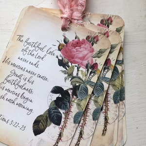 May include: Set of vintage-style gift tags with a pink rose illustration and script text. The tags are tied together with a pink ribbon. The text on the tags reads "The faithful love of the Lord never ends. His mercies never cease."