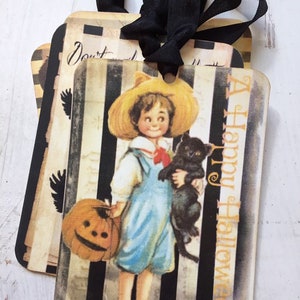 May include: Rectangular gift tags featuring a vintage illustration of a child in a straw hat holding a pumpkin and a black cat. The background has black and white vertical stripes with the text A Happy Halloween printed in orange on the side.