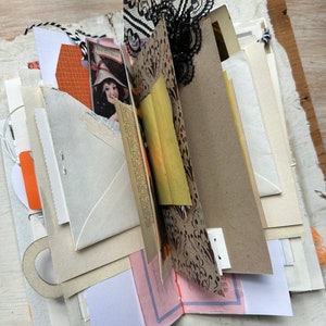 Puede incluir: Un diario artesanal con p&aacute;ginas superpuestas de diversas texturas y colores, incluyendo sobres color crema, cartulina naranja, papel estampado con motivos negros, una ilustraci&oacute;n de estilo vintage y detalles de encaje negro.