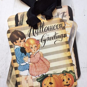 May include: A set of rectangular gift tags with black ribbon ties, featuring a vintage-style illustration of a child in a blue striped shirt and a child in a red checkered dress standing beside two orange jack-o'-lanterns with the text Halloween Greetings.