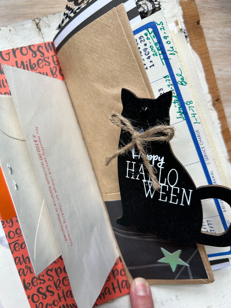 Puede incluir: Una silueta de gato de madera negra con un lazo de cuerda de yute y el texto blanco Happy HALLOWEEN, superpuesta sobre una colecci&oacute;n de ef&iacute;meros de papel vintage, incluyendo un extracto bancario con texto sobre cargos de servicio y un sobre de papel.