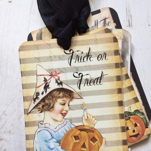 May include: A set of rectangular Halloween gift tags featuring a beige and brown striped background. The front tag displays a child in a witch hat holding a lit candle and a jack-o'-lantern, with the text Trick or Treat in black script.