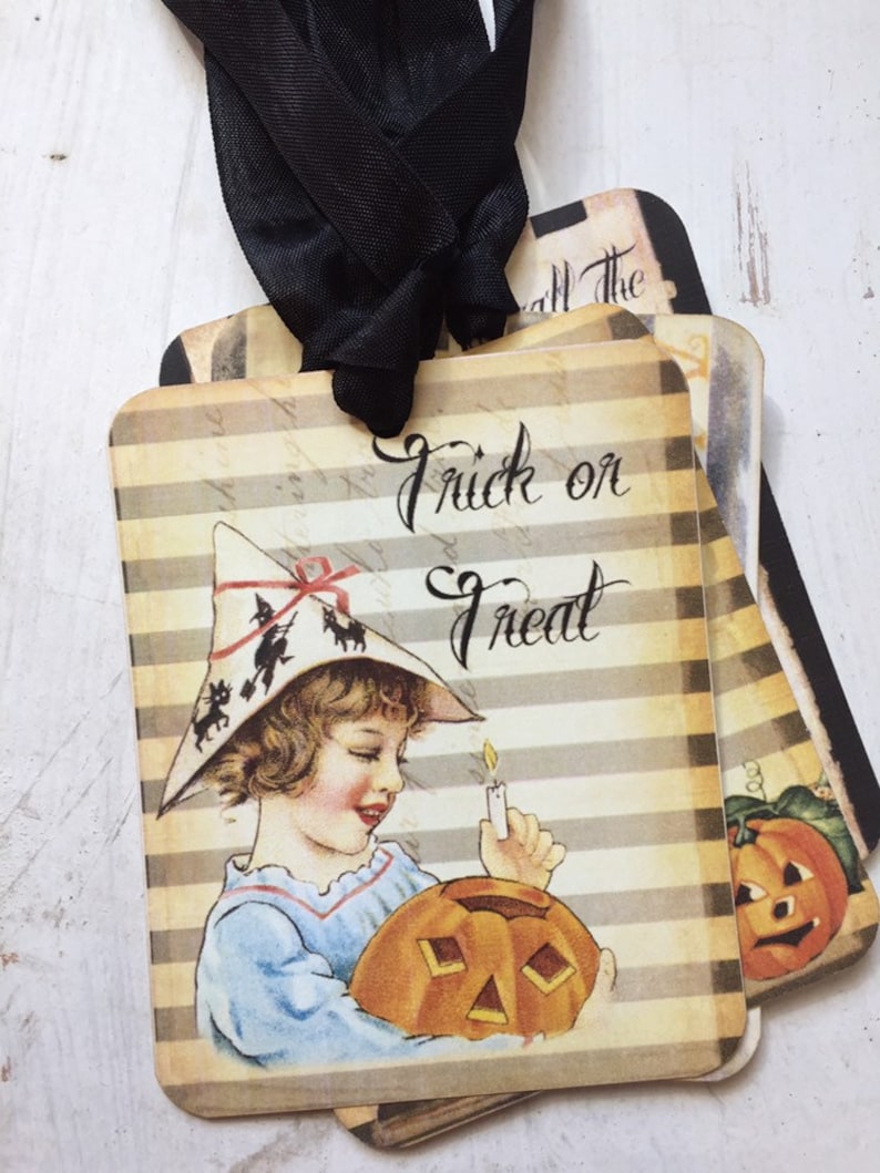 May include: A set of rectangular Halloween gift tags featuring a beige and brown striped background. The front tag displays a child in a witch hat holding a lit candle and a jack-o'-lantern, with the text Trick or Treat in black script.