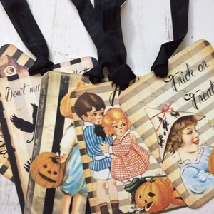 May include: Four rectangular paper tags with black ribbon loops, featuring vintage-style illustrations of children in costumes, pumpkins, and black stripes. One tag displays the text "Trick or Treat" and another shows "Don't make".