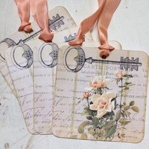 May include: Four vintage key-shaped gift tags with a floral design and handwritten text. The tags are tied with peach-colored ribbon.