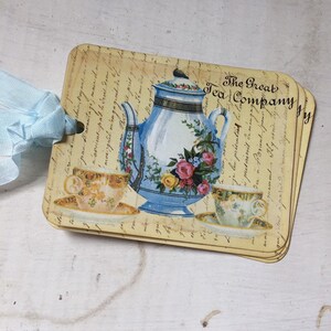 May include: A set of four vintage-style tea party gift tags featuring a blue and white teapot with floral accents and two teacups. The tags are printed with a script font and the text "The Great Tea Company".
