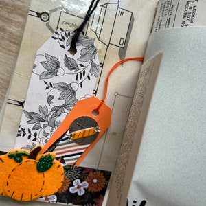 Puede incluir: Una p&aacute;gina de &aacute;lbum de recortes con una etiqueta floral en blanco y negro con cuerda negra, una etiqueta naranja con un adorno de caramelo, un recorte de calabaza de fieltro y una tira de papel floral. Incluye fragmentos de texto y la palabra Vibes!.