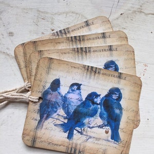 May include: A set of vintage-style gift tags featuring bluebirds perched on a branch. The tags are printed with a faded, distressed background and the text "UNION POSTALE UNIVERSIBILE" in multiple languages.