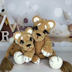 Puede incluir: Dos cachorros de le&oacute;n de peluche hechos a mano. Los leones son marrones con detalles blancos en las orejas, las patas y las caras. Tienen narices, pesta&ntilde;as y colas negras. Los cachorros est&aacute;n sentados juntos, creando una apariencia acogedora.
