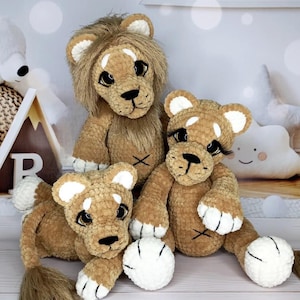 May include: Three handmade crochet lion soft toys. The lions are various sizes and have brown bodies, white paws, and white-tipped ears. The largest lion has a brown mane. Each lion has a black nose and eyes.
