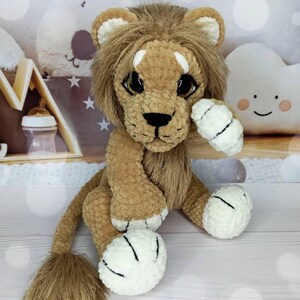 Puede incluir: Un juguete de le&oacute;n de peluche hecho a mano con melena, cuerpo y cola marrones. El le&oacute;n tiene ojos grandes y expresivos, una nariz negra y patas blancas con rayas negras. El juguete est&aacute; dise&ntilde;ado para parecerse a un cachorro de le&oacute;n amigable.