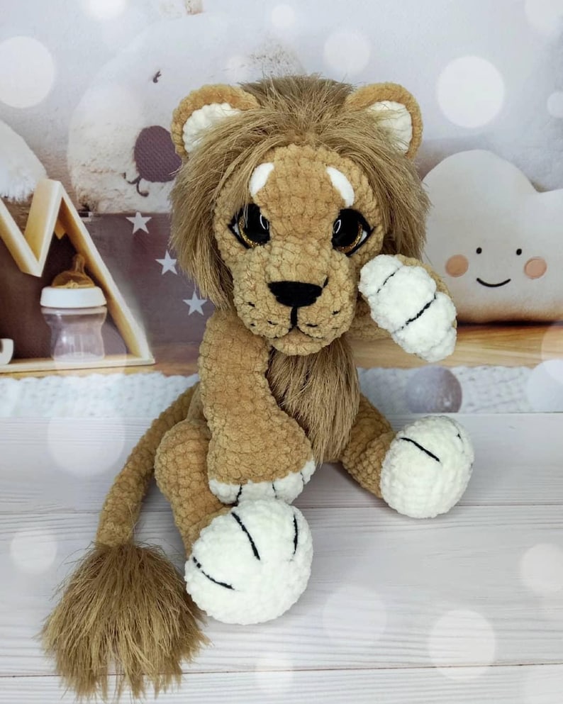 Puede incluir: Un juguete de le&oacute;n de peluche hecho a mano con melena, cuerpo y cola marrones. El le&oacute;n tiene ojos grandes y expresivos, una nariz negra y patas blancas con rayas negras. El juguete est&aacute; dise&ntilde;ado para parecerse a un cachorro de le&oacute;n amigable.