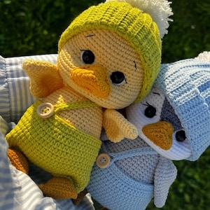 May include: Three handmade crochet duck toys. One is yellow with a green hat and dungarees, the other is grey with blue dungarees and a blue hat. All have button details. The third duck is yellow with a green hat and dungarees.
