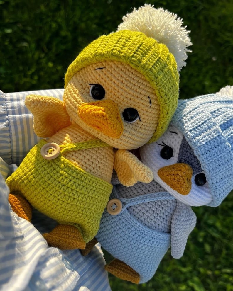 May include: Three handmade crochet duck toys. One is yellow with a green hat and dungarees, the other is grey with blue dungarees and a blue hat. All have button details. The third duck is yellow with a green hat and dungarees.