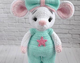 May include: A handmade crochet mouse doll with a white body, pink and white ears, and a mint green bow. The mouse wears a mint green jumpsuit with a pink star. The doll is a soft toy.