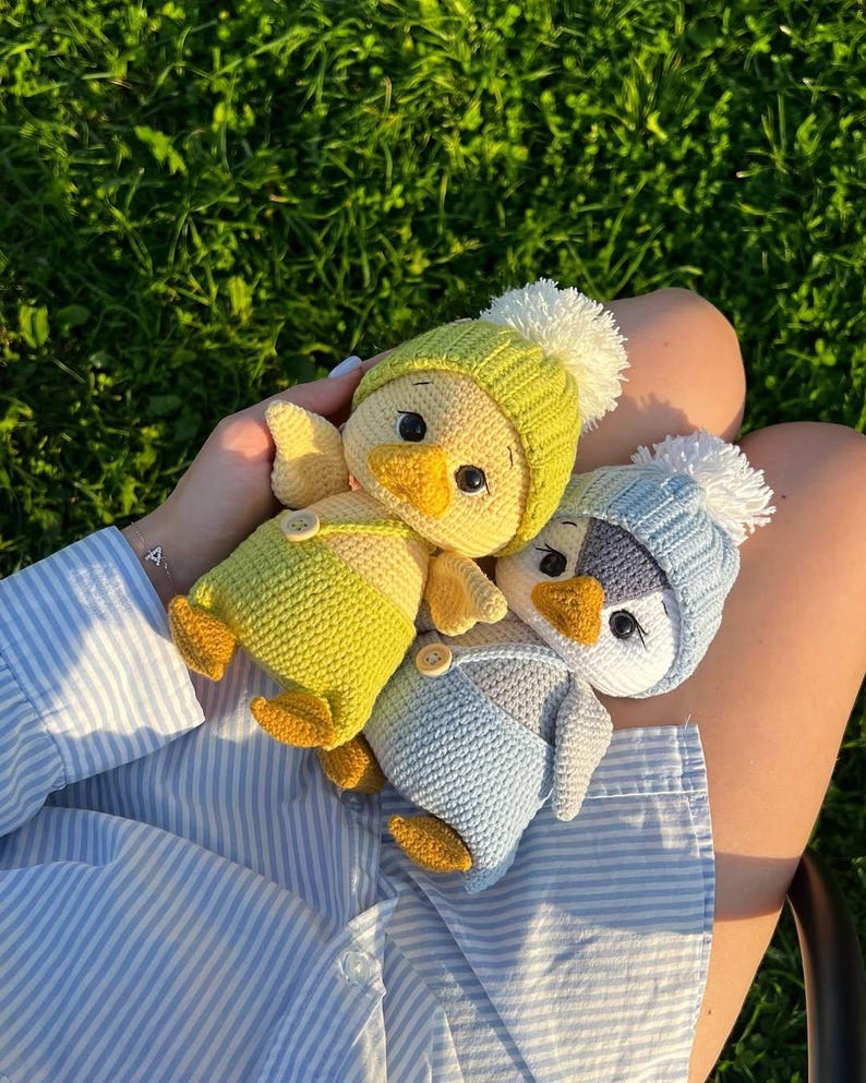 May include: Three crocheted chick toys, each wearing a hat with a white pom-pom and dungarees. One chick is yellow with a green hat, another is blue with a light blue hat, and the third is yellow with a light blue hat.