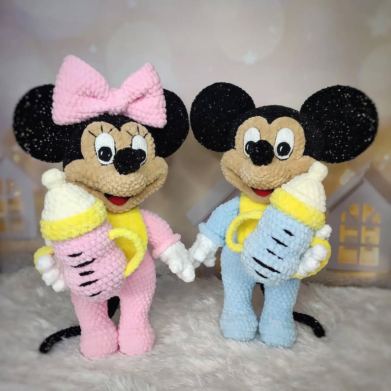 Puede incluir: Dos mu&ntilde;ecos de peluche de Mickey y Minnie Mouse, cada uno sosteniendo un biber&oacute;n. Minnie lleva un atuendo y un lazo rosa, mientras que Mickey est&aacute; en azul. Ambos tienen orejas negras, caras color canela y detalles amarillos.