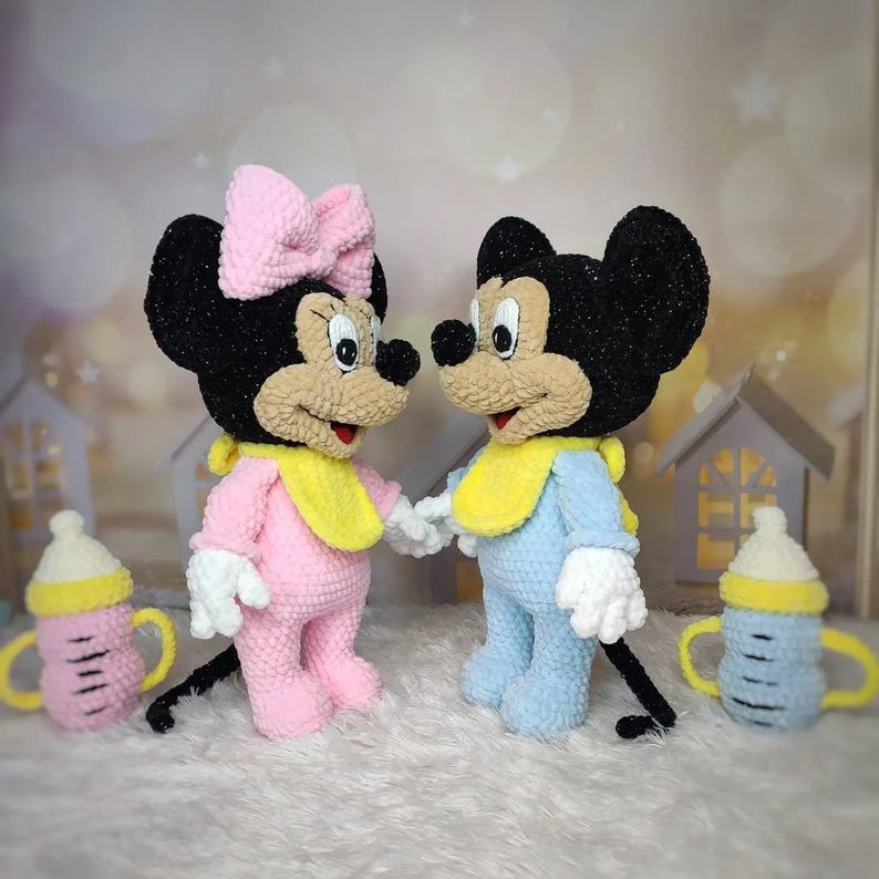 Puede incluir: Mu&ntilde;ecos de Mickey y Minnie Mouse tejidos a ganchillo, cada uno con un babero y ropa de beb&eacute;. Minnie lleva un conjunto rosa y un lazo, mientras que Mickey est&aacute; en azul. Tambi&eacute;n hay dos biberones a juego, uno rosa y otro azul.