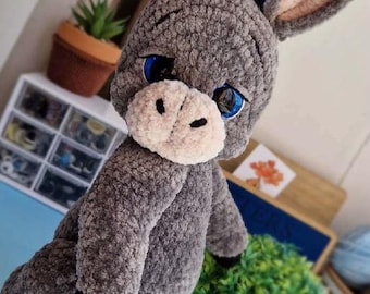 May include: A handmade gray plush donkey with large blue eyes, a white muzzle, and black hooves. The donkey has large, floppy ears with pink inner ears. The plush animal is a soft, cuddly toy.