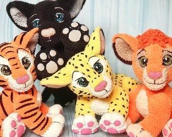 May include: A collection of handmade crochet animal plush toys. The toys include a black panther, a tiger with orange and black stripes, a yellow leopard with black spots, and an orange lion. Each toy has detailed features and is made with soft yarn.