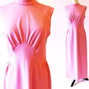 May include: A sleeveless pink maxi dress with a high mock neck and a fitted bodice. The dress has a unique design with a curved panel at the bust.